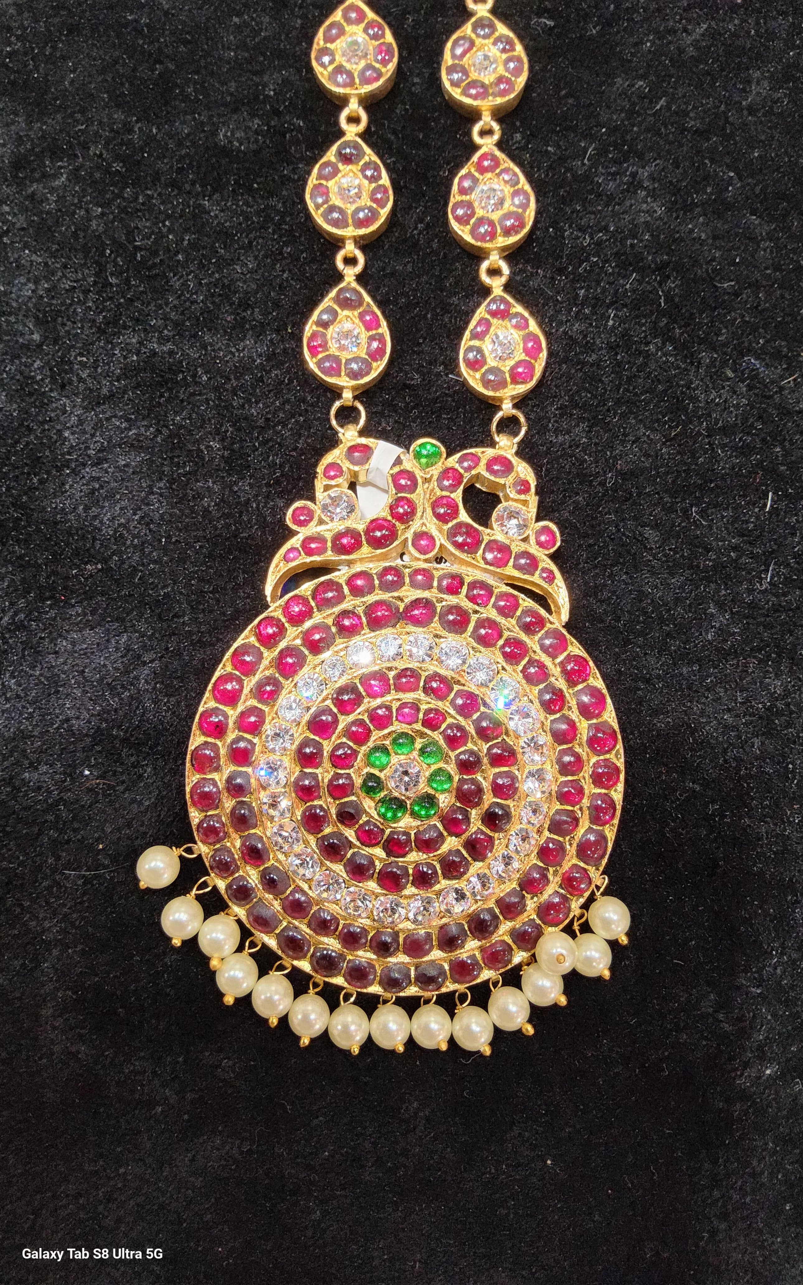 Close-up of Big Dollar Original Temple Jewellery, showing detailed craftsmanship of golden deity on dark fabric. Ethnic jewelry.
