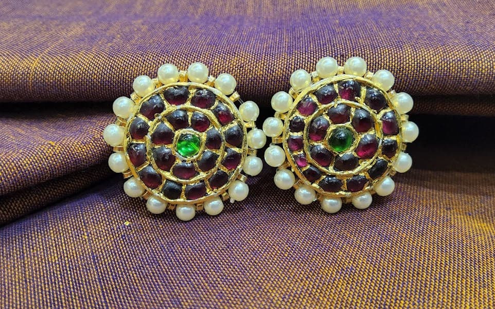 Close-up of temple jewellery stud jummiki. Silver base gold leaf, red and green kemp stones. Bharatanatyam jewellery.