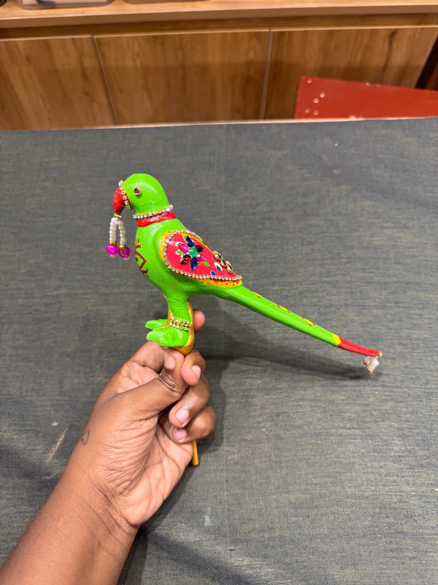 parrot accessory for Bharatanatyam dance, held by hand, against textile shelves.