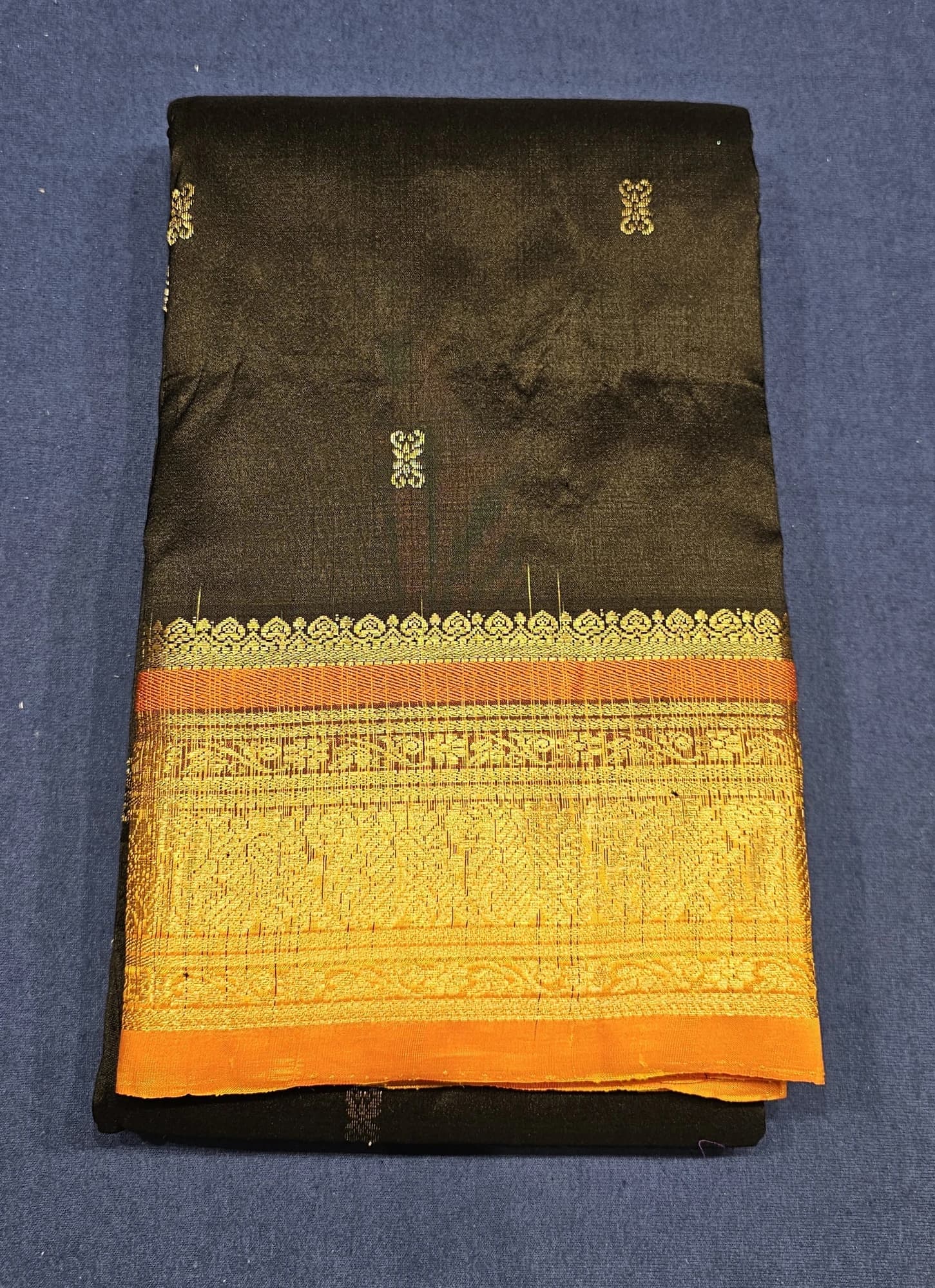 Black w Orange Dharmavaram Silk Saree, folded, displaying intricate gold weave motifs and a rich gold and orange border.
