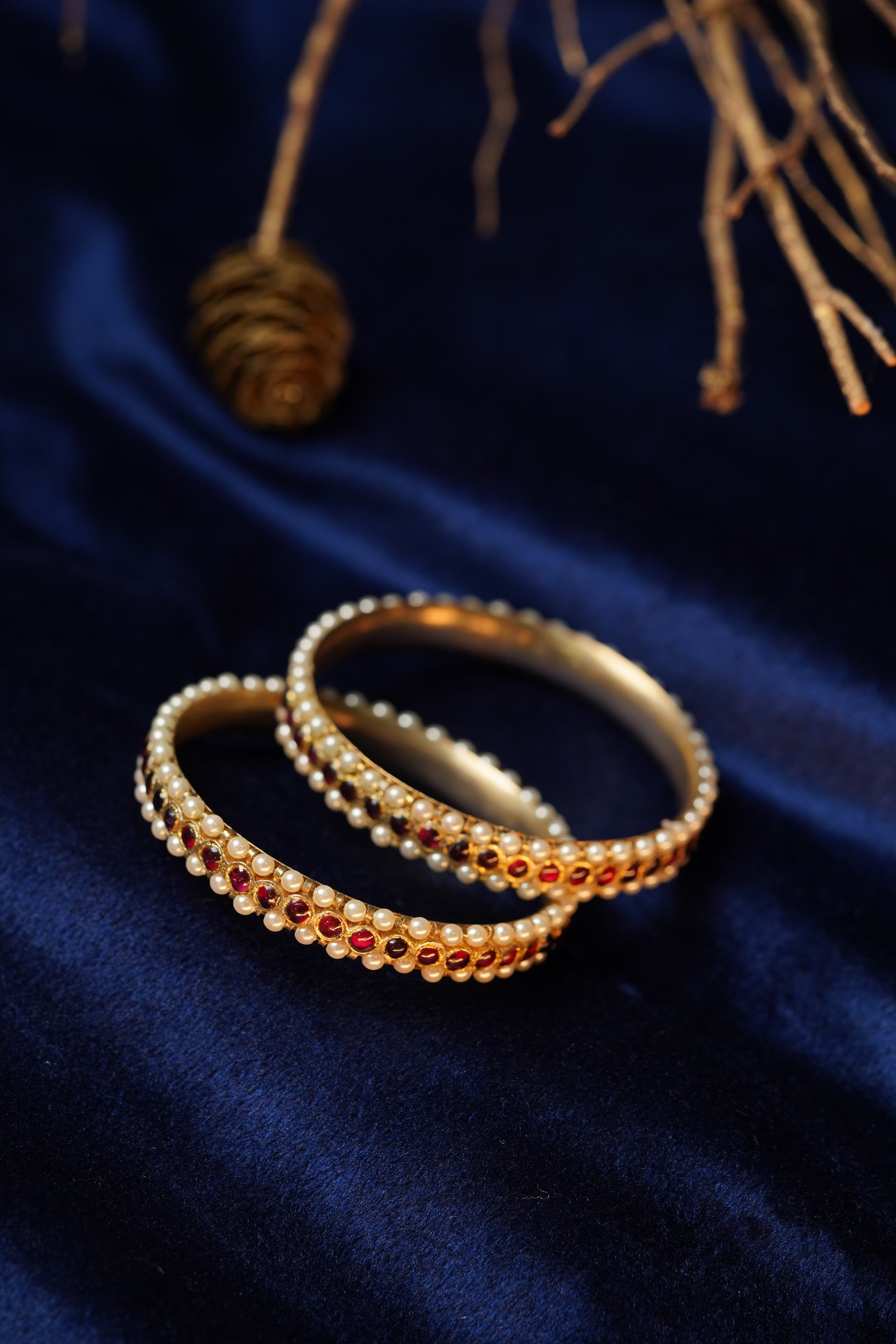 Close-up Pearl Bangle: Intricate pearl and maroon stone detailing on gold bangle for formal events