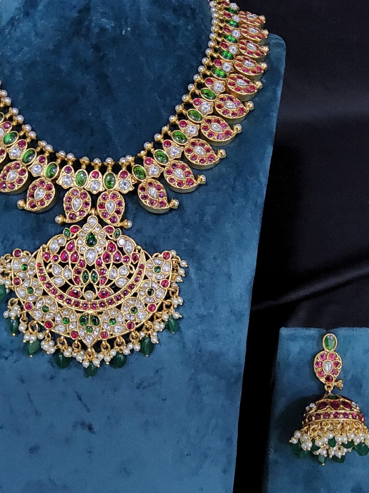 Side angle of Antique Mango Malai Set jhumkis: Copper based earrings with sparkling white, green, and red stones.