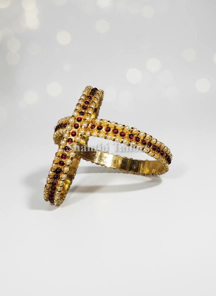 Thin imitation bangles in gold, featuring rows of red stones & white pearls, crossed.