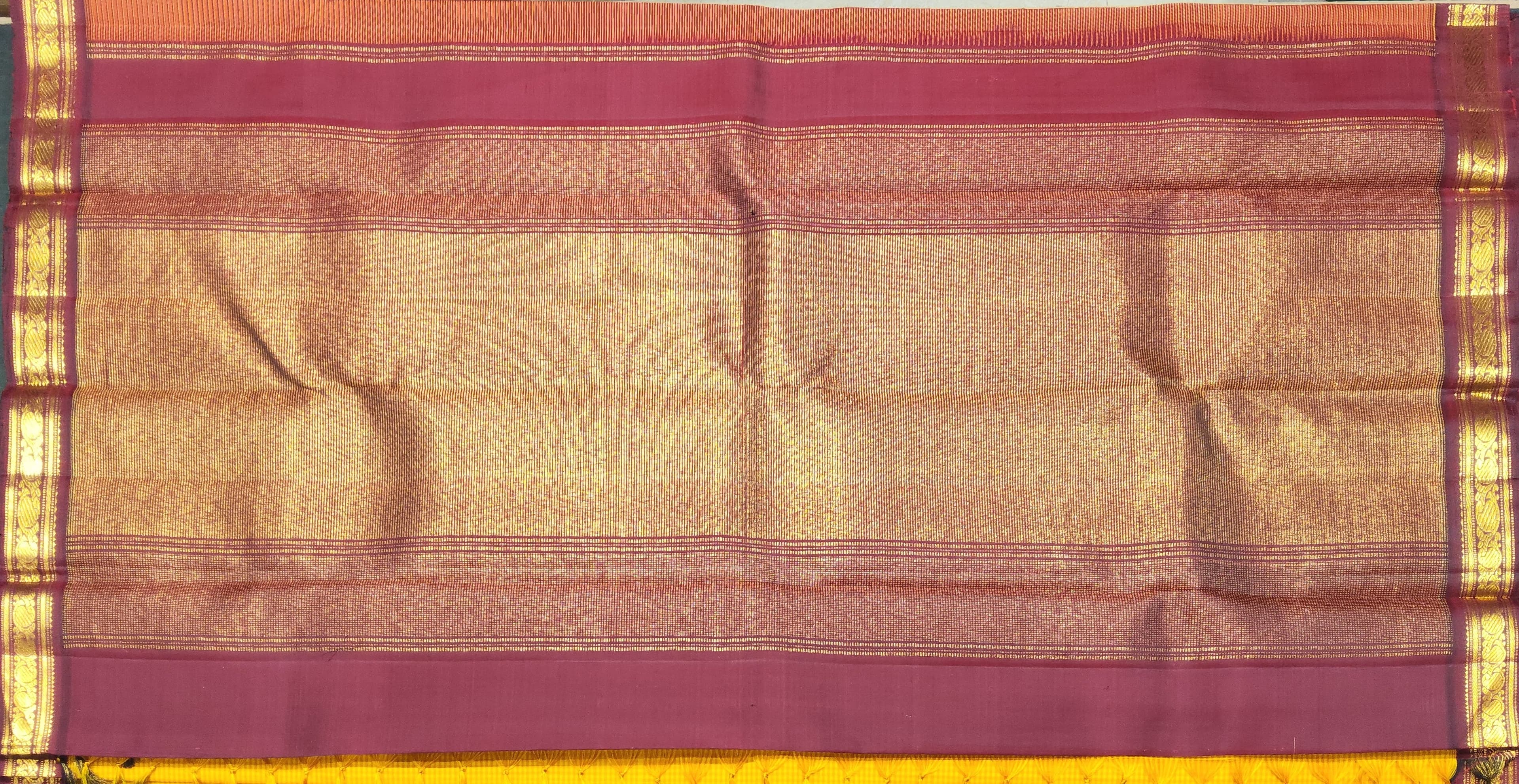 Close-up of Kanchipuram authentic silk saree's gold zari border. Mango yellow and maroon details.